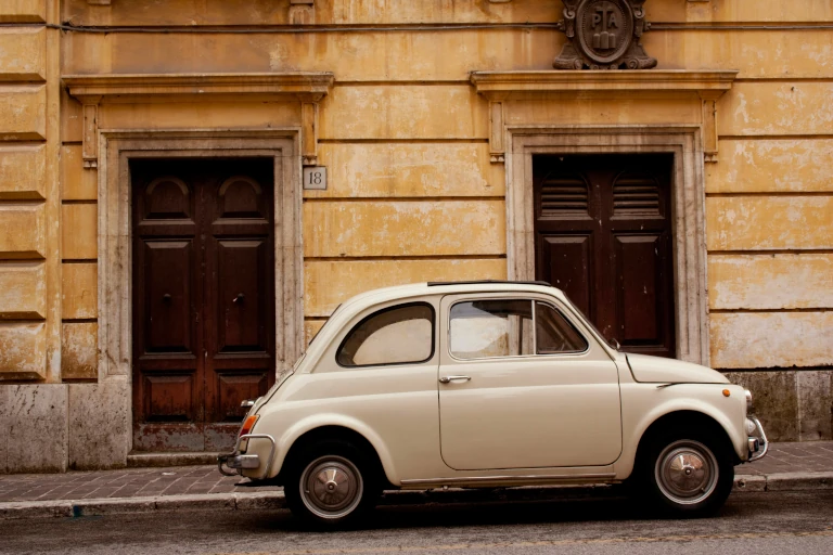 Photographie d'une ancienne Fiat 500 stationnée au pied d'un immeuble.